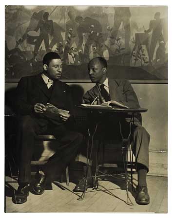 (THEATRE.) Frederick O'Neal and Abram Hill (?) seated in front of Aaron Douglas's mural at the Schomburg Center